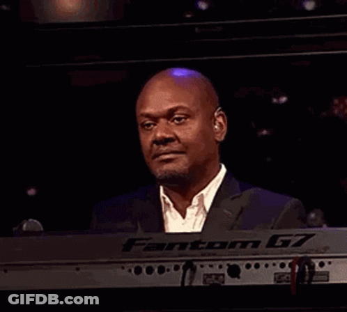 A Man In A Suit Is Laughing While Playing A Keyboard In A Dark Room . GIF