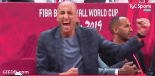 A Man In A Suit Is Laughing While Sitting In A Stadium . GIF