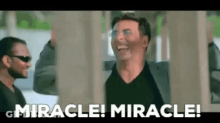A Man In A Suit Is Laughing While Standing Next To Another Man In Sunglasses . GIF