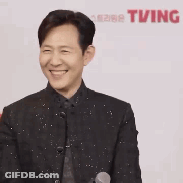 A Man In A Suit Is Laughing With His Eyes Closed And His Hands In The Air . GIF
