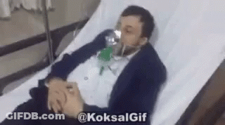 A Man In A Suit Is Laying In A Hospital Bed With An Oxygen Mask On His Face . GIF