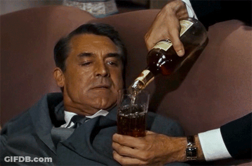 A Man In A Suit Is Laying On A Couch While Someone Pours A Drink Into A Glass GIF
