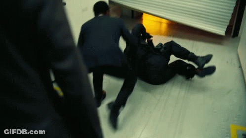 A Man In A Suit Is Laying On The Floor While Another Man Stands Behind Him GIF
