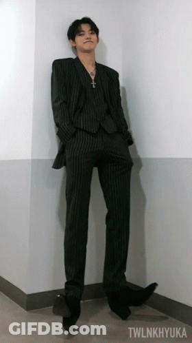 A Man In A Suit Is Leaning Against A Wall With Twlnkhyuka Written On The Bottom GIF