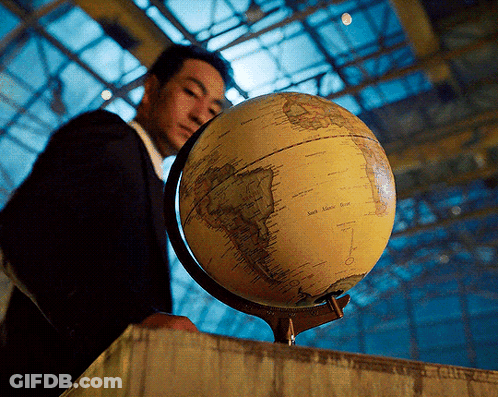 A Man In A Suit Is Looking At A Globe With The Words South America On It GIF