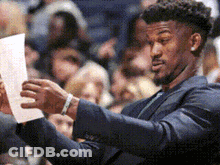 A Man In A Suit Is Looking At A Piece Of Paper . GIF