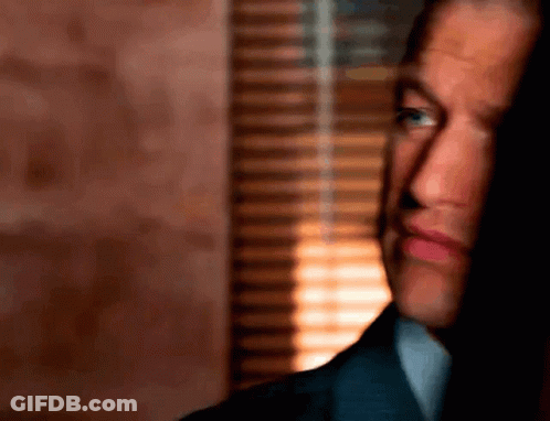A Man In A Suit Is Looking Out A Window GIF
