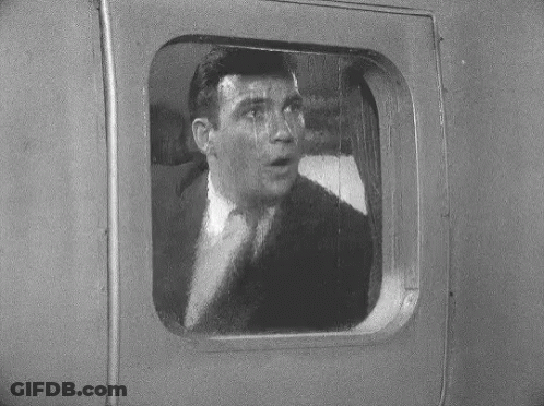 A Man In A Suit Is Looking Out Of A Window GIF