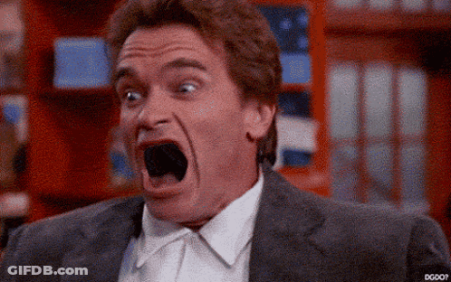A Man In A Suit Is Making A Funny Face With His Mouth Wide Open . GIF