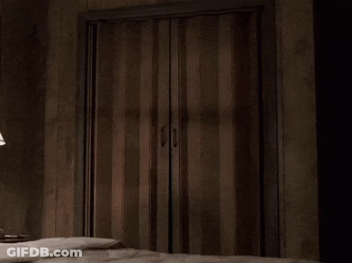 A Man In A Suit Is Peeking Out Of A Doorway GIF
