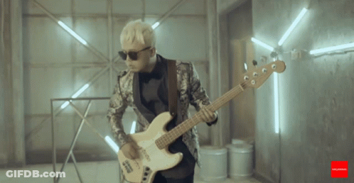 A Man In A Suit Is Playing A Guitar In A Room With Lights Behind Him GIF