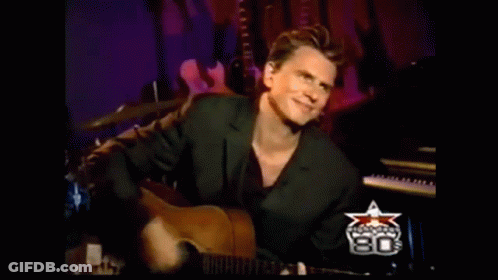 A Man In A Suit Is Playing A Guitar In Front Of A Sign That Says ' 80 ' On It GIF