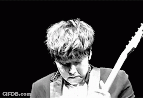 A Man In A Suit Is Playing An Electric Guitar On A Stage In A Black And White Photo . GIF