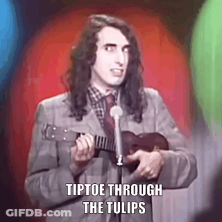 A Man In A Suit Is Playing An Ukulele In Front Of A Microphone . GIF