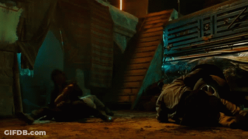 A Man In A Suit Is Pointing A Gun At Another Man In A Mask GIF
