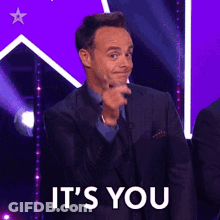 A Man In A Suit Is Pointing At The Camera With The Words It 'S You Behind Him GIF