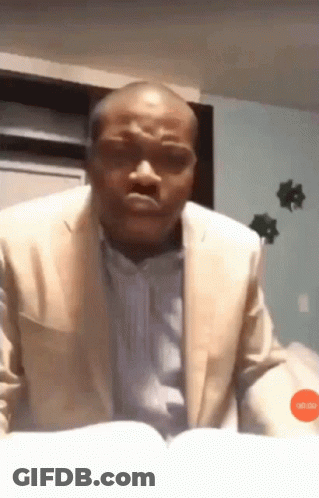 A Man In A Suit Is Reading A Book And Making A Face GIF