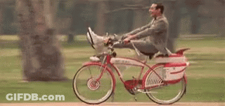 A Man In A Suit Is Riding A Bicycle With His Feet Up In A Park . GIF