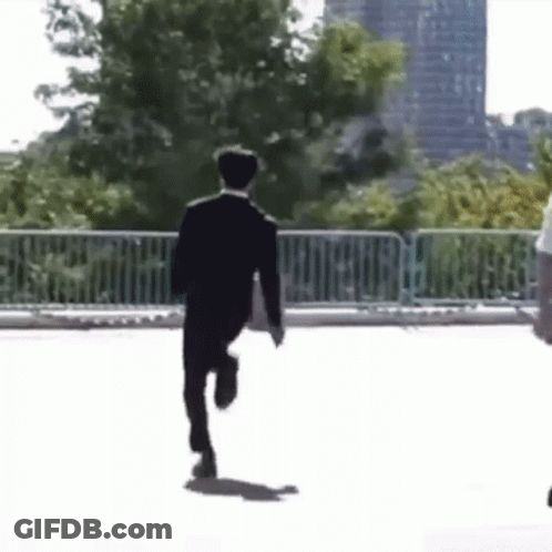 A Man In A Suit Is Running Down A Street Holding A Briefcase . GIF