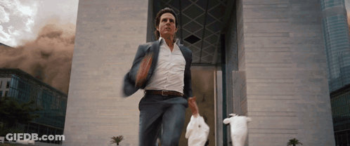 A Man In A Suit Is Running In Front Of A Building GIF
