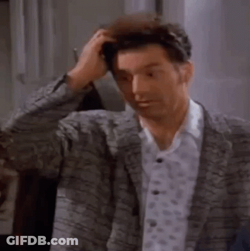 A Man In A Suit Is Scratching His Head While Standing In A Room . GIF
