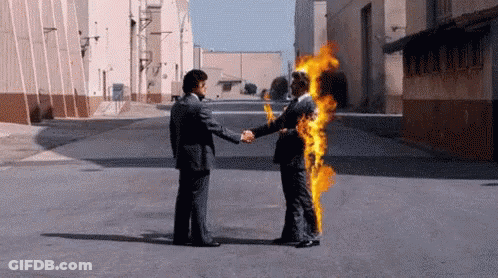 A Man In A Suit Is Shaking Hands With Another Man In A Suit Who Is On Fire . GIF