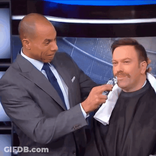 A Man In A Suit Is Shaving Another Man 'S Face With A Razor GIF