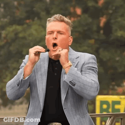 A Man In A Suit Is Singing Into A Microphone In Front Of A Yellow Sign That Says Re GIF