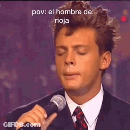 A Man In A Suit Is Singing Into A Microphone . GIF