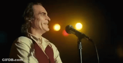 A Man In A Suit Is Singing Into A Microphone On A Stage . GIF