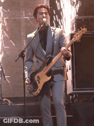 A Man In A Suit Is Singing Into A Microphone While Playing A Bass Guitar GIF