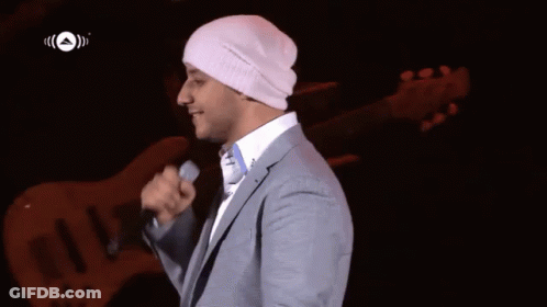 A Man In A Suit Is Singing Into A Microphone While Wearing A White Beanie GIF