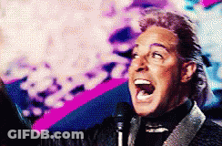 A Man In A Suit Is Singing Into A Microphone With His Mouth Open GIF