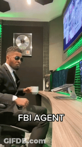 A Man In A Suit Is Sitting At A Desk With A Cup Of Coffee And The Words Fbi Agent Written On The Table GIF