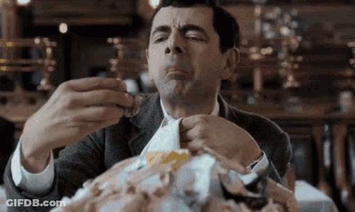 A Man In A Suit Is Sitting At A Table Eating A Large Amount Of Food . GIF