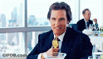 A Man In A Suit Is Sitting At A Table Holding A Trophy GIF