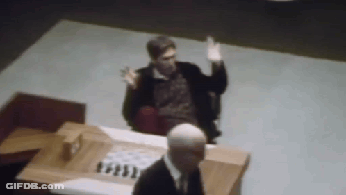 A Man In A Suit Is Sitting At A Table With A Chess Board In Front Of Him . GIF
