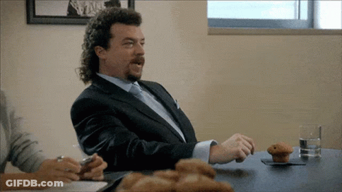 A Man In A Suit Is Sitting At A Table With A Muffin On It GIF