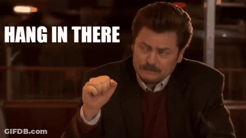 A Man In A Suit Is Sitting At A Table With His Fist In The Air And The Words `` Hang In There '' Behind Him . GIF