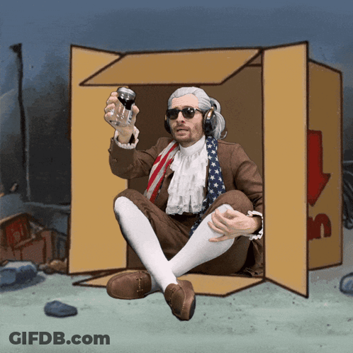 A Man In A Suit Is Sitting In A Cardboard Box Holding A Can Of Soda GIF