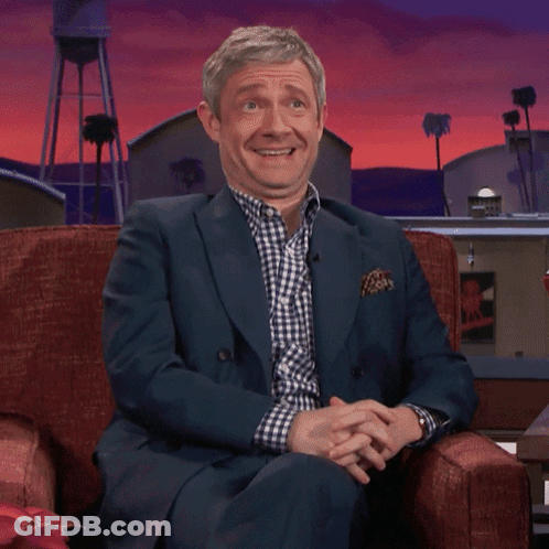 A Man In A Suit Is Sitting In A Chair And Laughing GIF