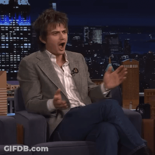 A Man In A Suit Is Sitting In A Chair And Making A Funny Face GIF