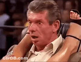 A Man In A Suit Is Sitting In A Chair With A Woman 'S Legs On His Shoulders . GIF