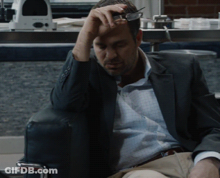 A Man In A Suit Is Sitting In A Chair With His Hand On His Forehead GIF