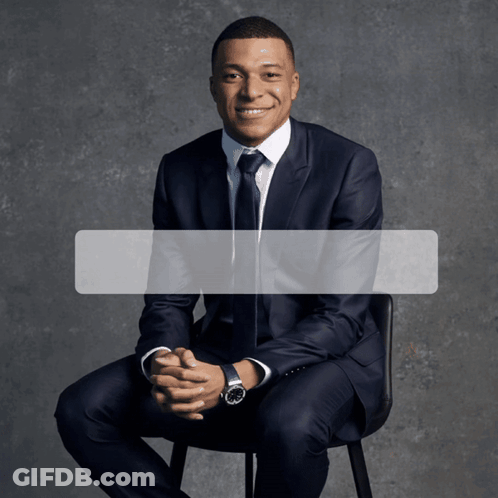 A Man In A Suit Is Sitting In A Chair With His Hands Folded GIF