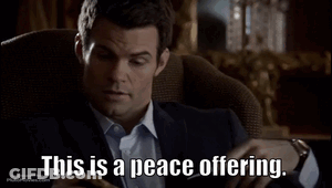 A Man In A Suit Is Sitting In A Chair With The Words This Is A Peace Offering GIF