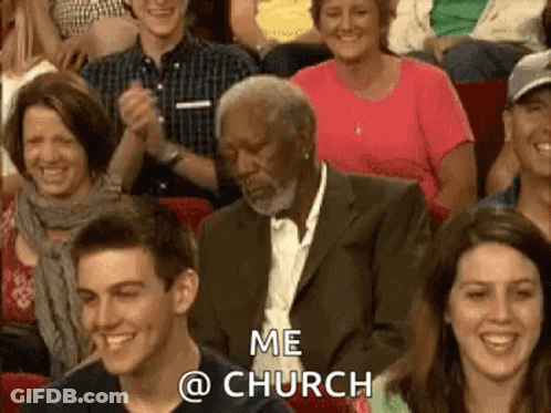 A Man In A Suit Is Sitting In A Crowd Of People Applauding And Laughing . GIF