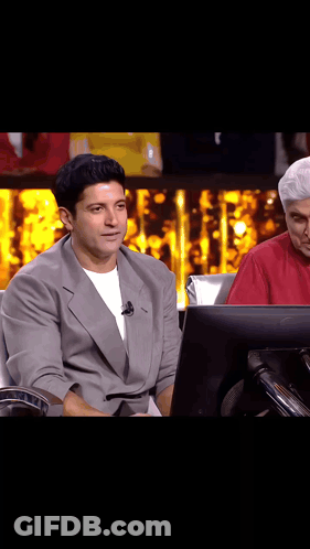 A Man In A Suit Is Sitting In Front Of A Computer Monitor On A Stage . GIF