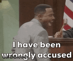 A Man In A Suit Is Sitting In Front Of A Judge Holding A Hammer . GIF