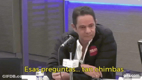 A Man In A Suit Is Sitting In Front Of A Microphone With The Words Esas Preguntas Tan Chimbas Written Below Him GIF